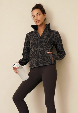 Black fleece jacket with a leopard print pattern, high collar, and zip closure, paired with black leggings and a clear water bottle.