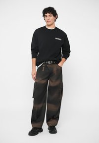 Černá mikina s logem "Double V", spárovaná s hnědými maskáčovými cargo kalhotami. Oblečení doplněno černými teniskami.