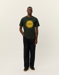 Tmavozelené bavlnené tričko s okrúhlym výstrihom a žltou grafickou potlačou s nápisom "LES DEUX" na prednej strane, kombinované so tmavými nohavicami a čiernymi topánkami.