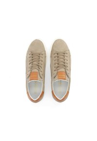 Baskets en suède beige avec un empiècement en cuir tan au niveau du talon, dotées de lacets plats et d'une semelle en caoutchouc blanche. À l'intérieur, étiquette en texte doré.