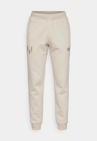 Beige Jogginghosen mit einer strukturierten Oberfläche. Ausgestattet mit einem elastischen Bund und schmal zulaufenden Beinen. Auffällige Logos auf dem linken Oberschenkel und der rechten Tasche.