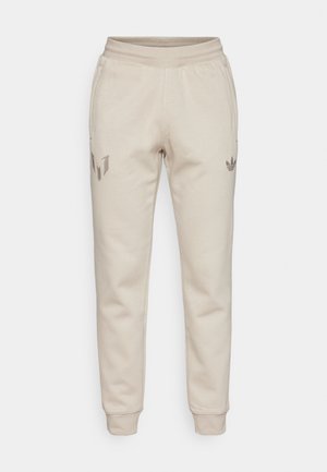 Biege sportinės kelnės su tekstūruotu paviršiumi. Turi elastingą juosmenį ir siaurėjančias kojas. Ryškūs logotipai kairiajame šlaunies ir dešinėje kišenėje.