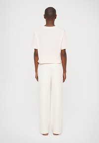 Tricou scurt de culoare roz deschis, cu mâneci scurte, asociat cu pantaloni albi, evazați. Textură netedă; design simplu, fără cusături.