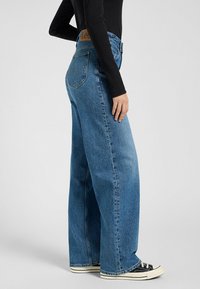 Weite blaue Jeans mit hohem Bund, ausgestattet mit einem braunen Lederlogo-Patch auf der Rückseite und einem klassischen Fünf-Taschen-Design.