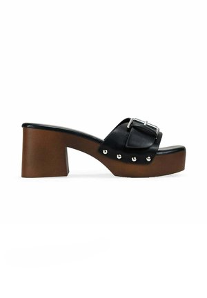 Sandalia de piel negra tipo slide con una correa ancha y hebilla plateada, plataforma marrón de tacón bloque con tachuelas plateadas a lo largo del lateral.