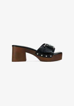 Sandalia de piel negra tipo slide con una correa ancha y hebilla plateada, plataforma marrón de tacón bloque con tachuelas plateadas a lo largo del lateral.