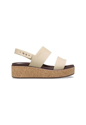 Beige platform sandals with cork sole, wide cross straps, and adjustable ankle strap. Features smooth material and modern design.