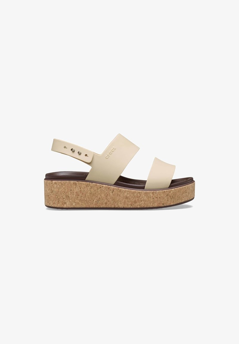 Beige platform sandals with cork sole, wide cross straps, and adjustable ankle strap. Features smooth material and modern design.