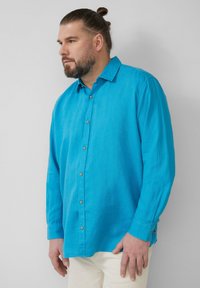 Turquoise shirt met lange mouwen en een kraag, knoopsluiting aan de voorkant en een ontspannen pasvorm, gemaakt van lichtgewicht stof met zichtbare stiksels.