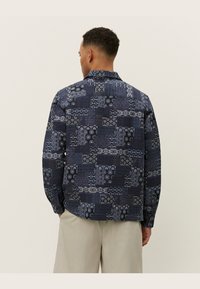 Navy shirt with a varied pattern of squares and intricate designs, featuring a standard collar and buttoned front, made from textured fabric.