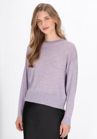 Maglione lungo a maniche con una vestibilità rilassata di colore viola chiaro, con polsini e orlo a coste, mostrato su una gonna nera contro uno sfondo neutro.