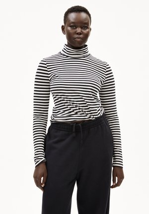 Zwart-wit gestreepte coltrui met een knoopdetail in de taille, gecombineerd met losse, donkergrijze joggingbroeken.