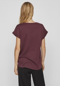 Bordeauxfarbenes T-Shirt mit entspannter Passform, kurzen aufgerollten Ärmeln und rundem Halsausschnitt, aus weichem Baumwollmaterial. Die Rückansicht zeigt eine glatte Textur.