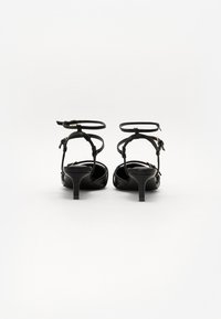 Sandales à talons hauts en cuir noir avec des brides de cheville, présentant une finition lisse et des talons blocs fins, conçues pour des occasions formelles.