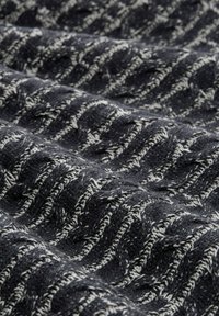 Dunkelgrauer gestrickter Stoff mit einem welligen, strukturierten Muster und kontrastierenden weißen Akzenten, die ein weiches, geschichtetes Erscheinungsbild erzeugen.