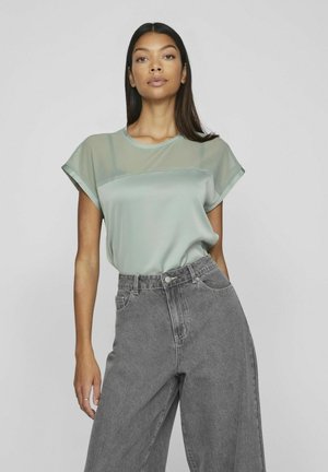 Light green short-sleeve top with a sheer overlay design, paired with high-waisted gray denim wide-leg jeans. Smooth fabric, casual fit.
