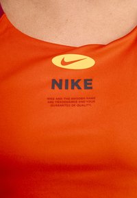 Red athletic top featuring a rounded neckline, a large yellow Nike logo, and bold black text stating "NIKE" on the front, smooth texture.