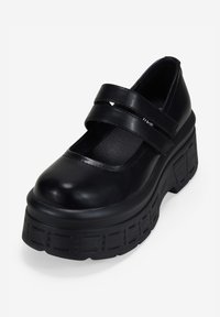 Zapato Mary Jane negro de plataforma con dos correas de velcro y suela gruesa y texturizada, en ángulo para mostrar el frente y el lado exterior.