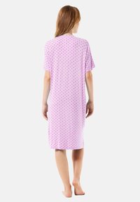 Camisón rosa de manga corta, diseño de longitud media, con un pequeño patrón de corazones negros en toda la prenda. Tejido suave y corte relajado.