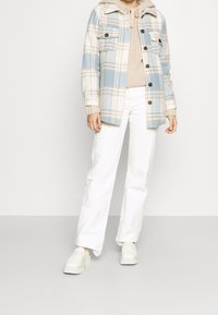 Blauw en crèmekleurig geruit jasje met twee borstzakken, beige gebreide trui, witte rechtlopende broek en witte platform sneakers.