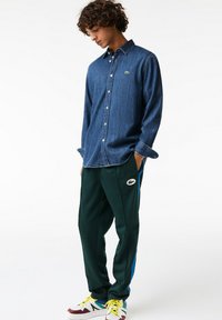 Granatowa koszula typu button-up z denimu, zestawiona z zielonymi spodniami dresowymi z niebieskimi paskami po bokach i logo. Białe i bordowe buty sportowe.