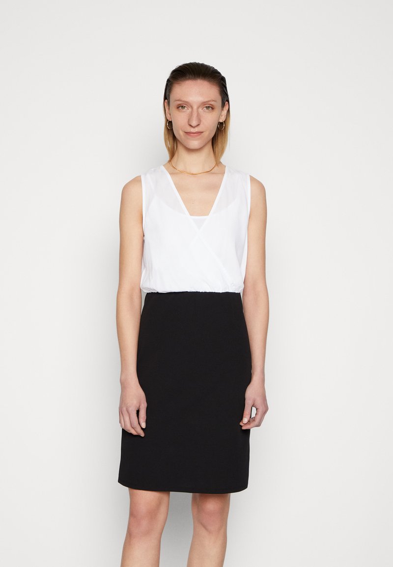 Vestido sem mangas com parte de cima branca e decote em V, e saia preta até ao joelho. Fabricado em diferentes texturas de tecido, com acabamento suave.