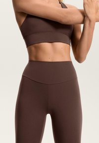 Smeđa sportska grudnjak i odgovarajuće visokog struka tajice od glatkog, rastezljivog materijala. Minimalistički dizajn s bešavnim šavovima i bez uzoraka.
