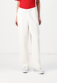 Vita linnebyxor med vida ben och elastiskt midjeband, med en slät yta och en avslappnad passform. Parat med vita sneakers.