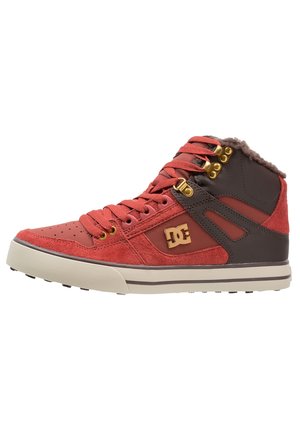 High-top DC sneaker in rood en donkerbruin met gouden veterogen, rode veters en een beige zool, met een fleece gevoerde kraag.