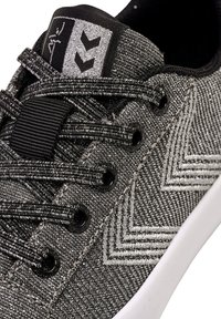 Schwarze und silberne Sneaker mit strukturiertem Stoff, Zickzackmuster, schwarzen Ösen und Schnürsenkeln. Weiße Gummisohle. Markenlogo auf der Zunge.