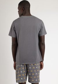 Camiseta de algodón gris con mangas cortas, con un cuello redondo clásico; combinada con pantalones cortos grises adornados con patrones repetidos en amarillo y blanco.