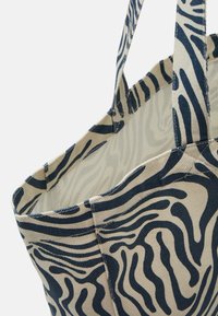 Sac fourre-tout en toile avec un motif zèbre crème et bleu marine. Dispose de poignées solides et d'une ouverture supérieure pour un accès facile.