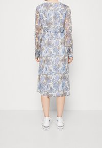 Sininen paisleymuotoilun midi-mekko, jossa on pitkät läpinäkyvät hihat ja kootut vyötäröllä, yhdistettynä valkoisiin lenkkareihin.