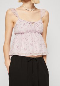 Ljuslila blus i polyester med blommönster, volangband, knytband vid halsringningen och en luftig, lös passform. Bärs med svarta byxor.