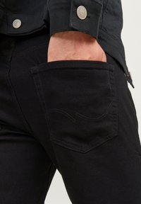 Jeans de mezclilla negra con un corte recto. Bolsillo delantero visible con un patrón de costura sutil. La tela presenta una textura suave y durabilidad.