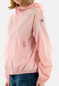 Giacca a vento leggera rosa con cappuccio, polsini e vita elasticizzati. Caratterizzata da una tasca frontale con zip e un logo sulla manica.