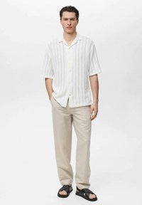 Witte kortekoope shirt met verticale strepen, gecombineerd met lichtbeige broeken en zwarte sandalen voor een casual look.