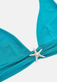 Teal színű bikini felső, csavart kialakítással, középen csillagpolip díszítéssel, amelyet rhinestone kövek ékesítenek. Simának tűnő anyagtextúra.