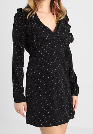 Zwarte jurk met lange mouwen en kleine witte polka dots, V-hals en gerimpelde details op de schouders en borst.