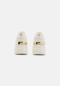 Le sneakers platform bianche presentano una parte superiore in sintetico liscia, un accento dorato sul tallone e un design minimalista con retro arrotondato.