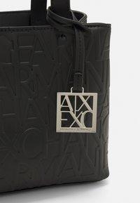Borsa tote nera con motivo a logo embossato, texture liscia e un'etichetta metallica argentata con il nome del marchio.