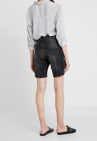 Svarta denimshorts med en slitna finish, kombinerade med en randig långärmad skjorta. Tyget är mjukt och passformen är avslappnad.