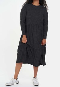 Robe à manches longues en coton gris foncé, à côtes, avec une conception à volants, atteignant le milieu du mollet, assortie à des chaussures de sport blanches. Tissu doux et texturé.