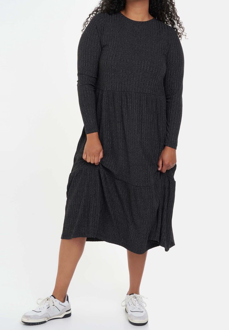 Robe à manches longues en coton gris foncé, à côtes, avec une conception à volants, atteignant le milieu du mollet, assortie à des chaussures de sport blanches. Tissu doux et texturé.