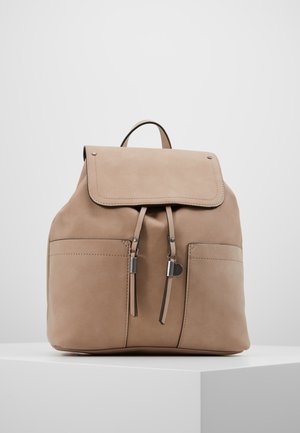Beige ruskindsrygsæk med flaplukning, to frontlommer og justerbare skulderremme. Har metallic hardware-accente.