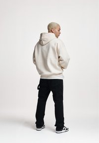 Light beige hoodie with a drawstring hood, paired with black cargo pants. Footwear features a white and black design. Simple, modern fit.