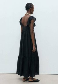 Robe maxi noire avec des manches courtes à volants, dos nu et bas à volants. Confectionnée dans un tissu léger avec une texture douce.