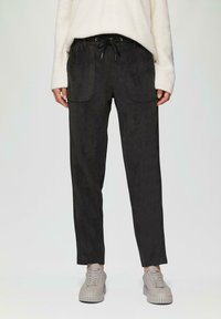 Zwarte broek met een gladde textuur, voorzien van twee voorzakken en een verstelbare broekband met trekkoord, gecombineerd met grijze sneakers.