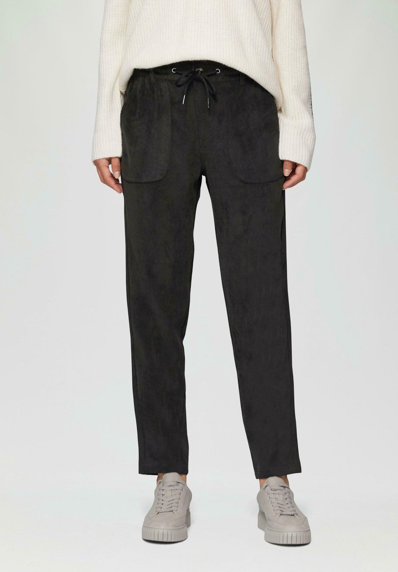 Zwarte broek met een gladde textuur, voorzien van twee voorzakken en een verstelbare broekband met trekkoord, gecombineerd met grijze sneakers.