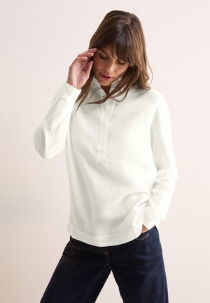 Pull en maille blanc à manches longues avec un col et un plastron de boutons. Fabriqué à partir d'un tissu texturé, associé à un jean en denim foncé.